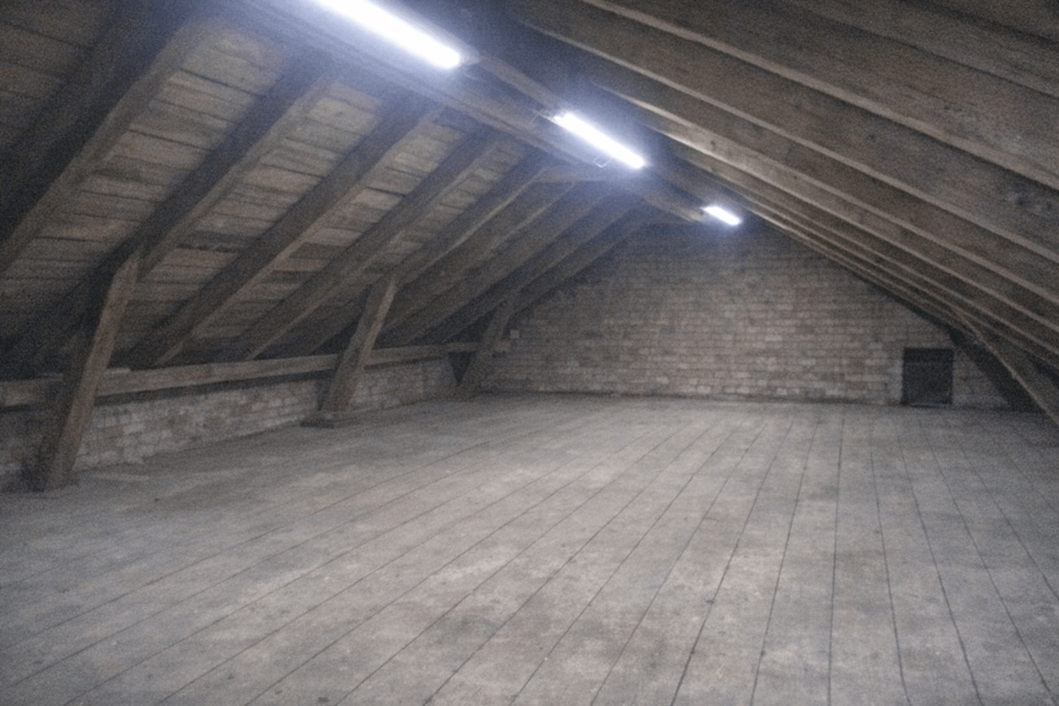 Freigeräumter Dachboden mit sichtbaren Holzbalken und gefegtem Boden